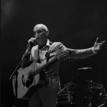 A photo of Paul Kelly singing and playing guitar